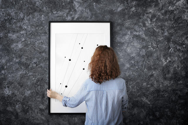 Woman hanging blank photo frame on dark wall print