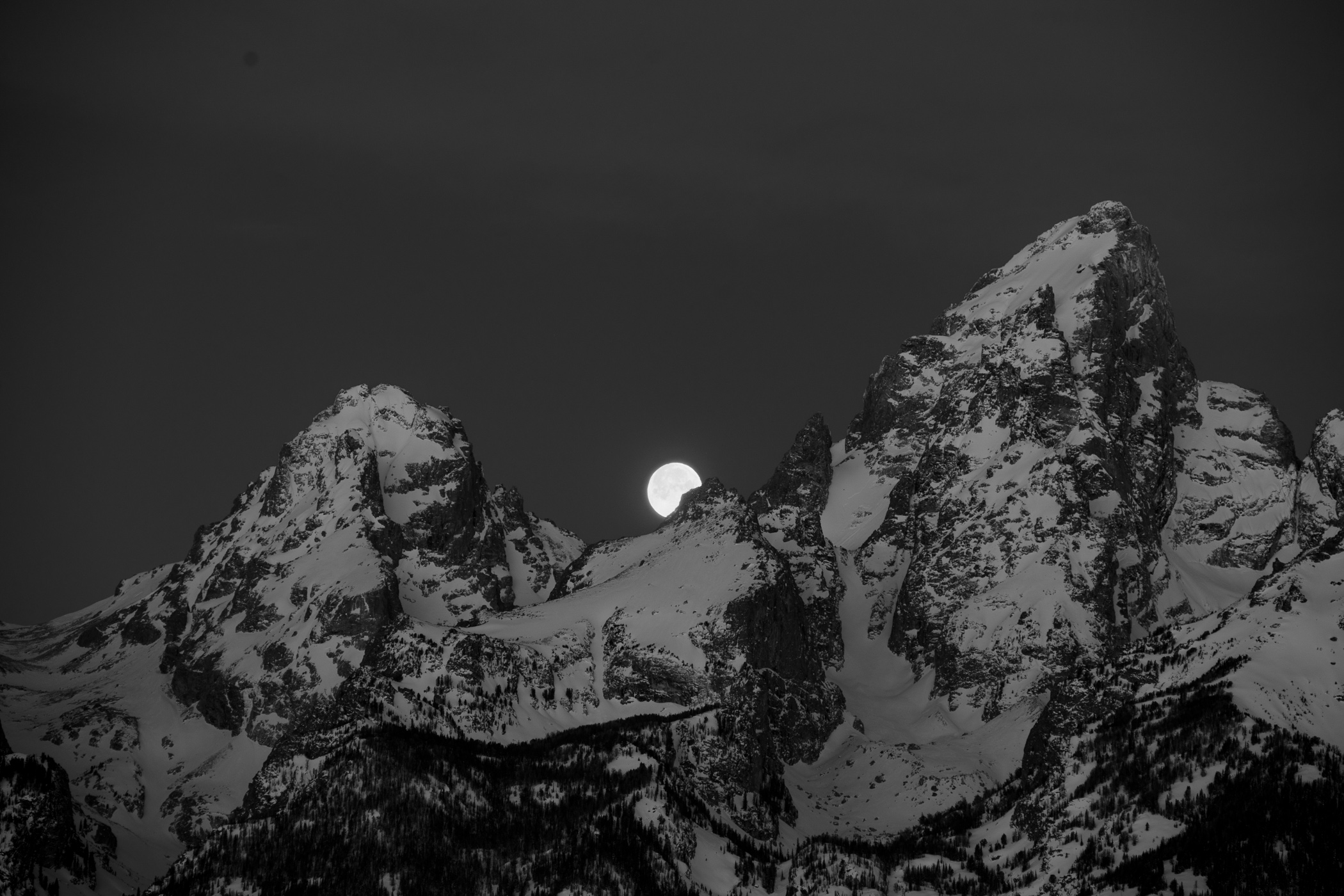 An early photo made of the moon setting between the mountain peaks